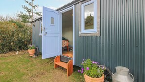 A small, single-story building with a blue door, a window, and a bench outside. - Skye (Ludlow)