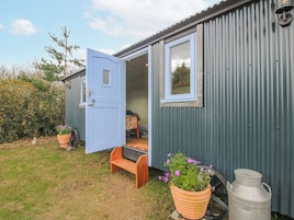 A small, single-story building with a blue door, a window, and a bench outside.