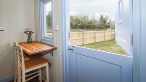 A room with a wooden table and chairs, a vase with flowers, a door leading outside, and a view of a wooden fence. - Skye (Ludlow)