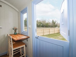 A room with a wooden table and chairs, a vase with flowers, a door leading outside, and a view of a wooden fence.