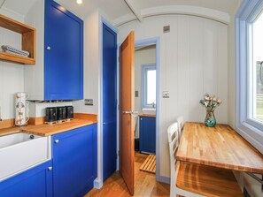 A compact kitchen with blue cabinets, a wooden countertop, a sink, and a dining area with a table and chairs. - Skye (Ludlow)