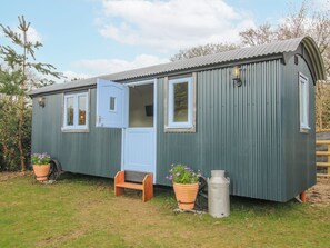 A small, single-story, metal-framed mobile home with a blue door, two windows, and a small porch area. - Skye (Ludlow)