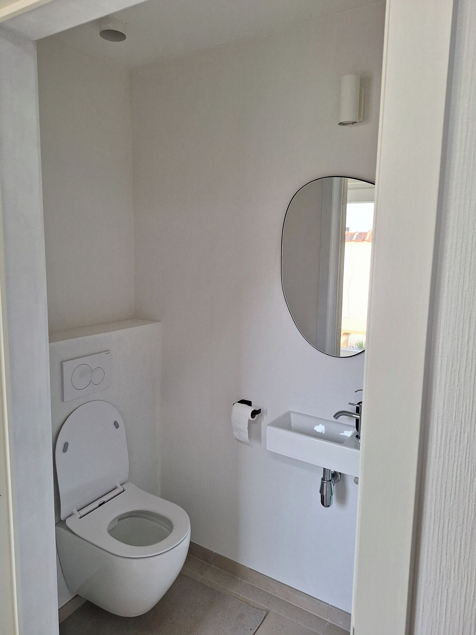 A small, modern bathroom with a toilet, a sink, and a mirror.