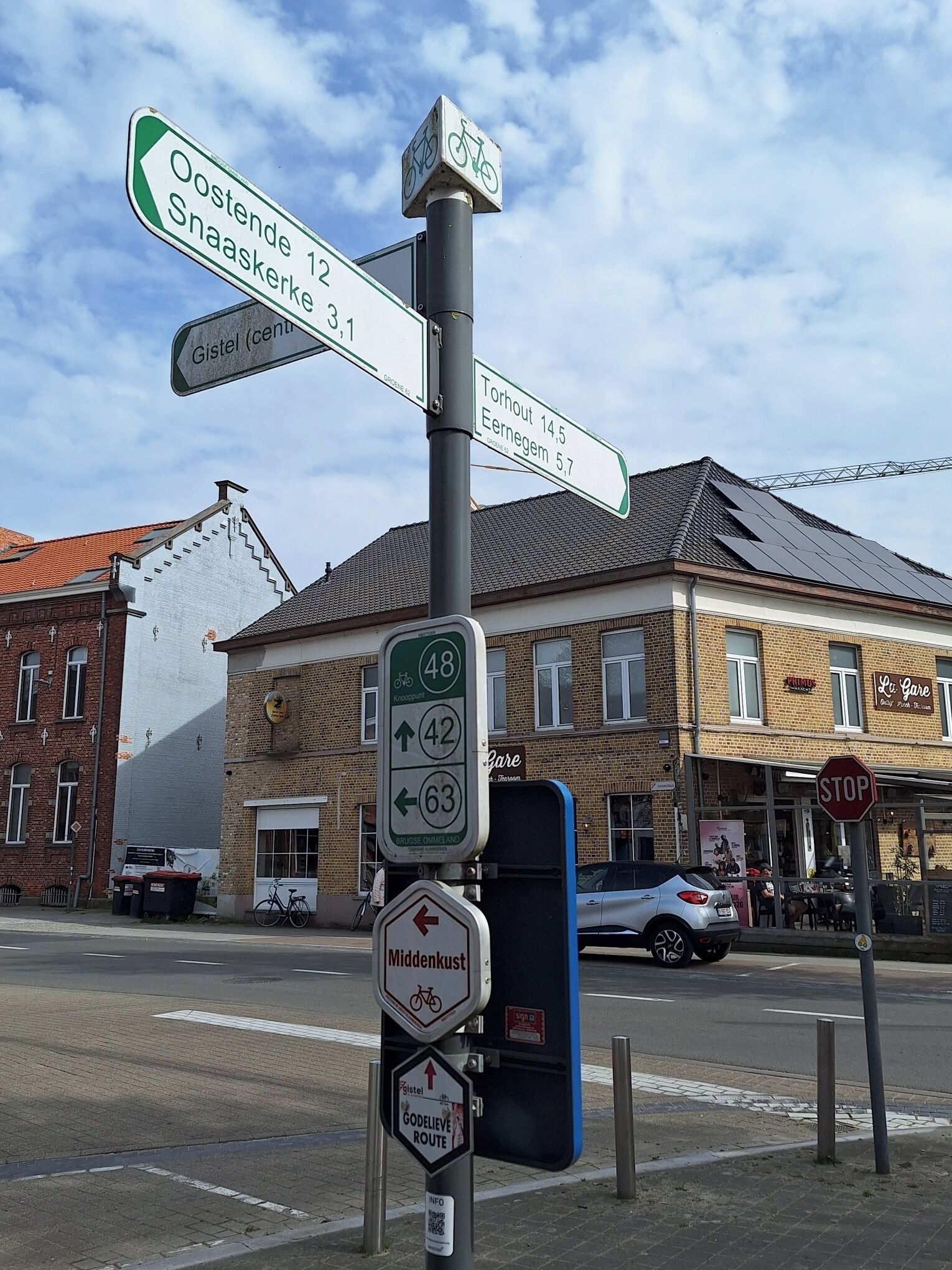 A street sign with directions to Oostende, Snaaskerke, Gistel, Torhout, Eernem, Middelkust, and a bike route.