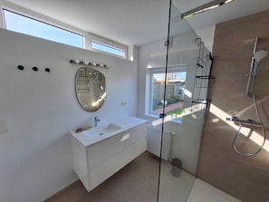 Een moderne badkamer met een grote spiegel, een witte wastafel, een douchegedeelte en een raam voor natuurlijk licht.