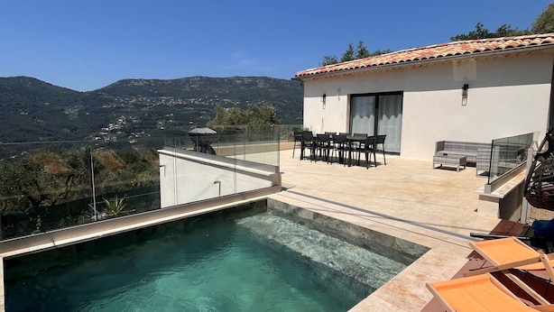 Uma piscina com água cristalina, rodeada por um deck com espreguiçadeiras e uma mesa.