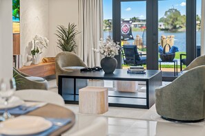 Ein modernes Wohnzimmer mit einem Glastisch, zwei Sesseln, einer Couch und Blick auf einen See mit Booten.