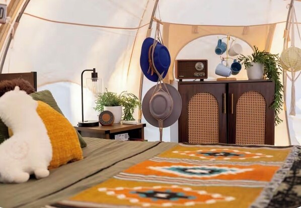 A cozy tent interior with a bed, a radio, and a cabinet with hanging items.