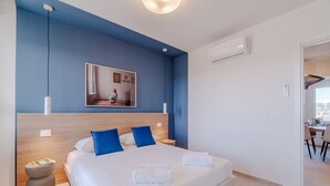 Una moderna camera d'hotel con un letto grande, una testiera in legno, un comodino, uno specchio fissato alla parete e vista sulla sala da pranzo.