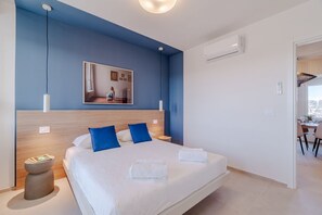 Ein modernes Hotelzimmer mit einem großen Bett, einem Holzkopfende, einem Nachttisch, einem wandmontierten Spiegel und Blick auf den Speisesaal.