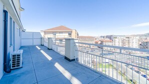 Un balcone con vista sulla città, un edificio dal tetto rosso e un cielo azzurro limpido.
