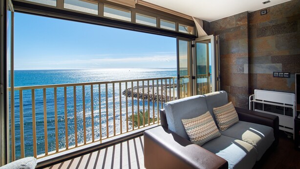 Ein Balkon mit Blick auf den Ozean, ein Sofa mit Kissen und ein weißer Nachttisch.