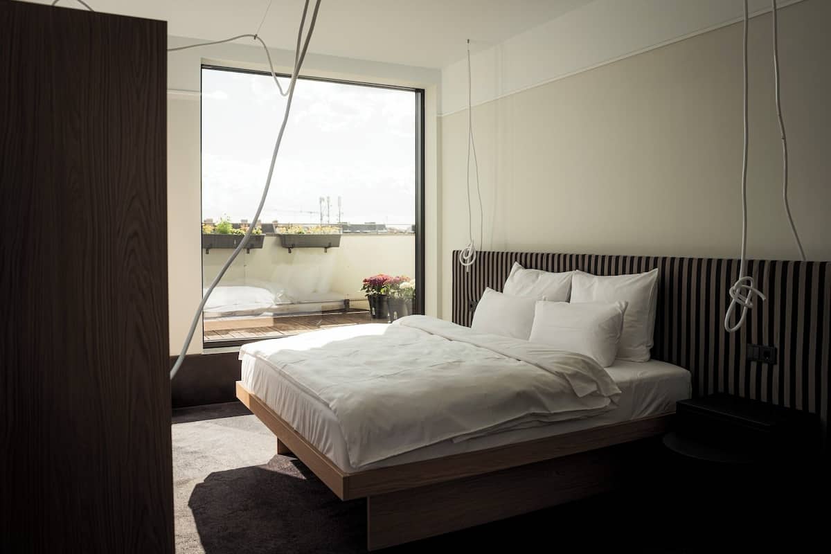 A modern bedroom with a large window, a bed with white linens, and a view of the cityscape.