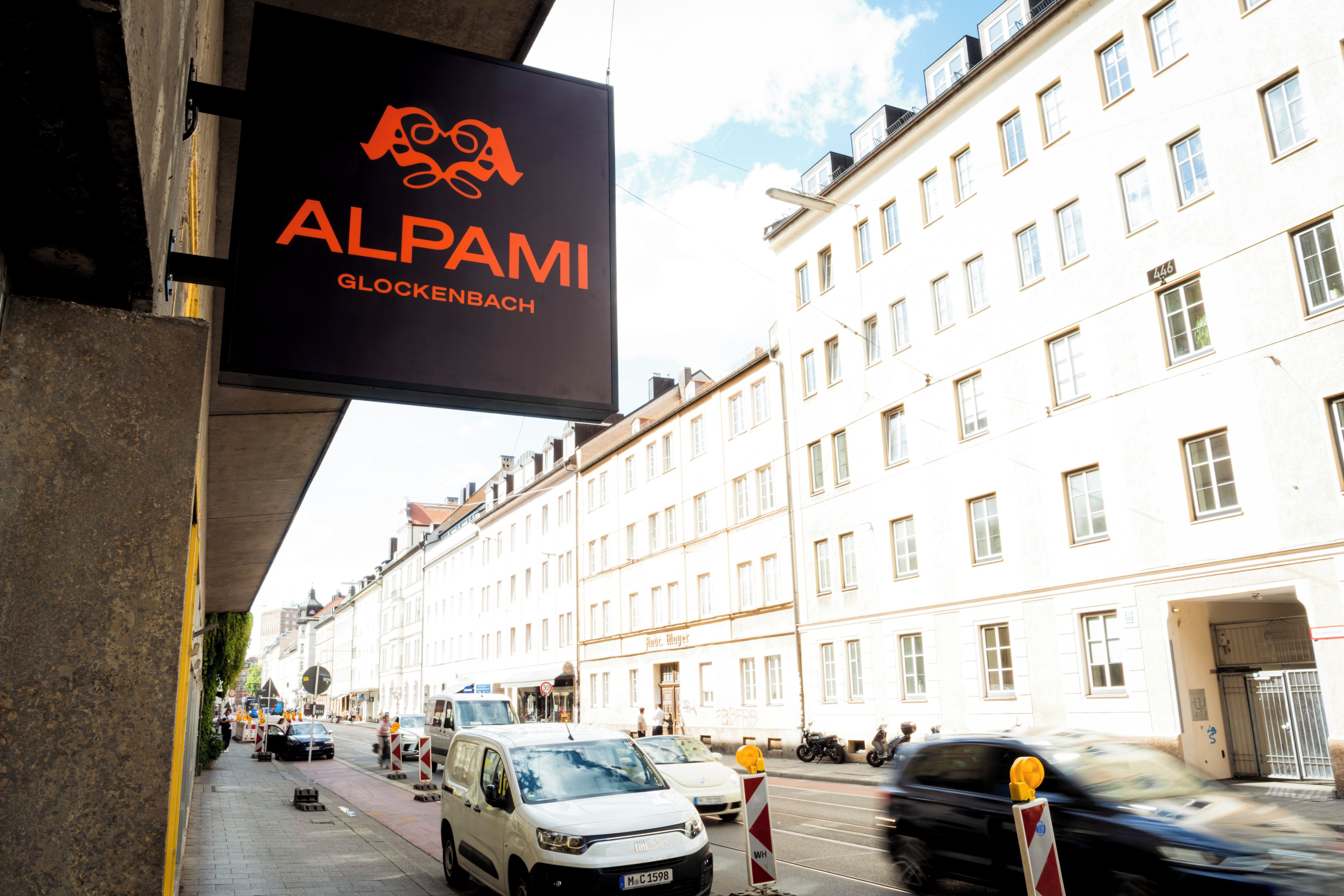 A street view with a building labeled 'ALPAMI GLOCKENBACH' and a white van parked on the street.