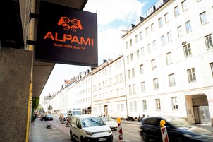 Vista de la calle con un edificio identificado como 'ALPAMI GLOCKENBACH' y una camioneta blanca estacionada.