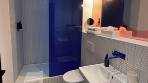 Un baño moderno con ducha a ras de suelo, inodoro, lavabo con espejo y toallero.