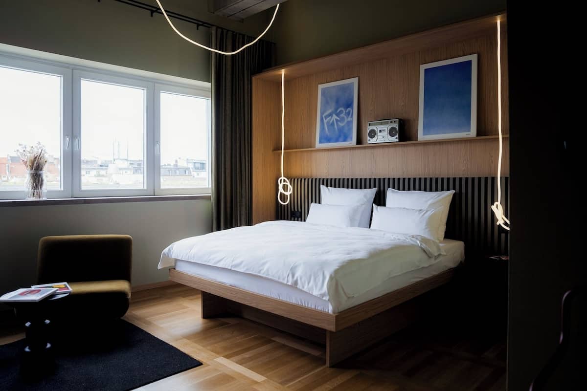 Quarto de hotel moderno com uma cama grande, uma mesa de trabalho e vista para a cidade.