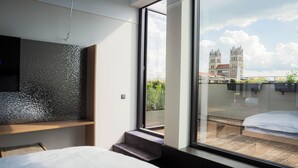 A modern hotel room with a large window, a bed, a TV, and a view of a historic building. - ALPAMI Glockenbach  (Munich)