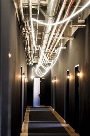 A hallway with a carpeted floor, a door at the end, and overhead pipes. - ALPAMI Glockenbach  (Munich)