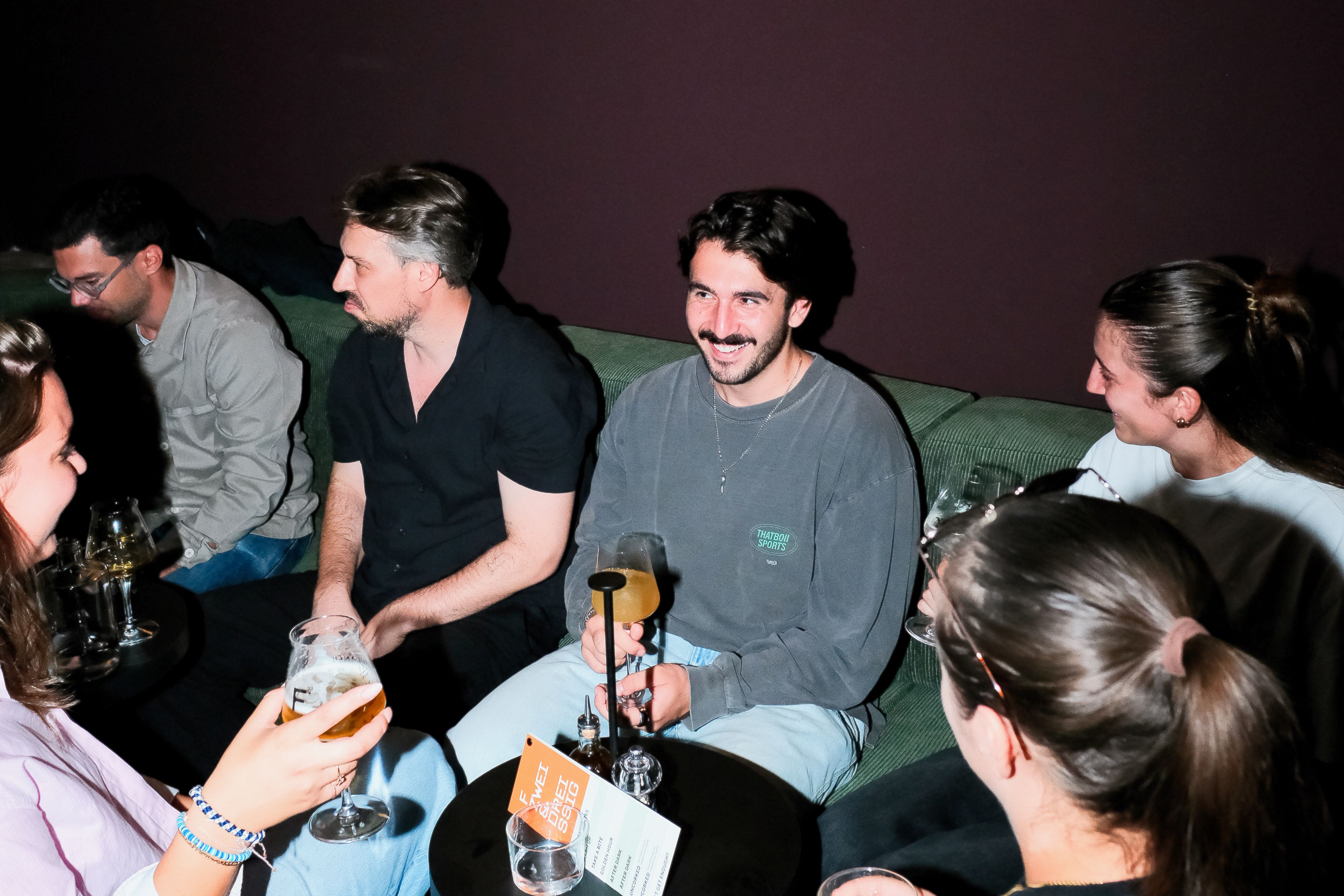 Eine Gruppe von Personen sitzt auf einem Sofa in einem schwach beleuchteten Raum.