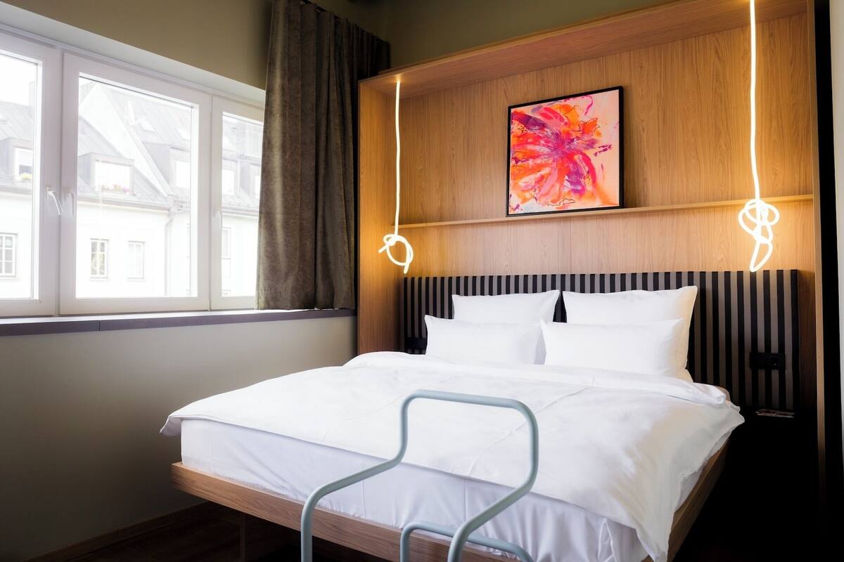Quarto de hotel com cama, janela, quadro e abajur.