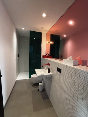 A modern bathroom with a white sink, a red faucet, a glass shower enclosure, and a mirror with a pink accent wall. - ALPAMI Glockenbach  (Munich)