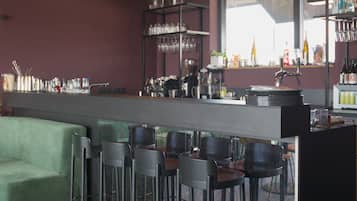 Una zona de bar con taburetes, una barra y estanterías con botellas y vasos.