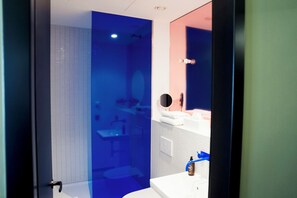 A modern bathroom with a glass shower enclosure, a sink with a blue faucet, and a mirror with a round frame. - ALPAMI Glockenbach  (Munich)
