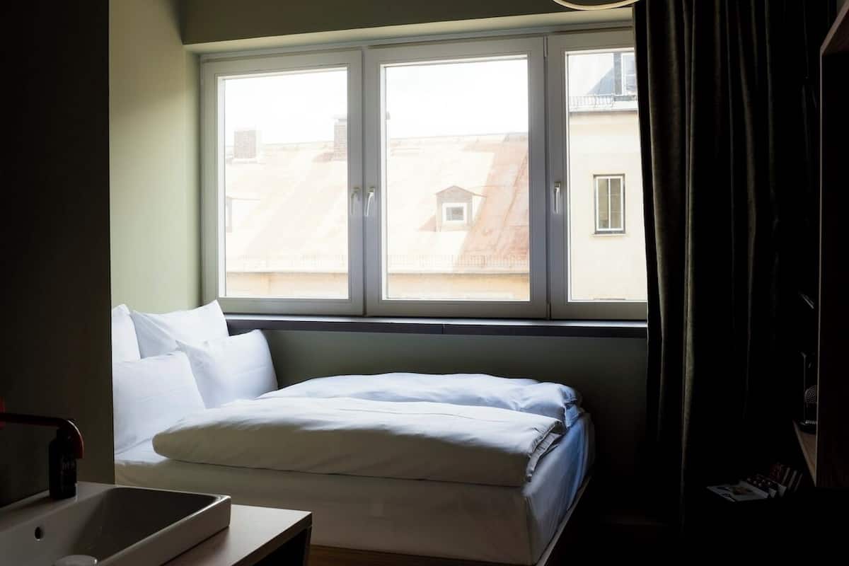 Quarto com cama, mesa de cabeceira, janela e luminária suspensa.