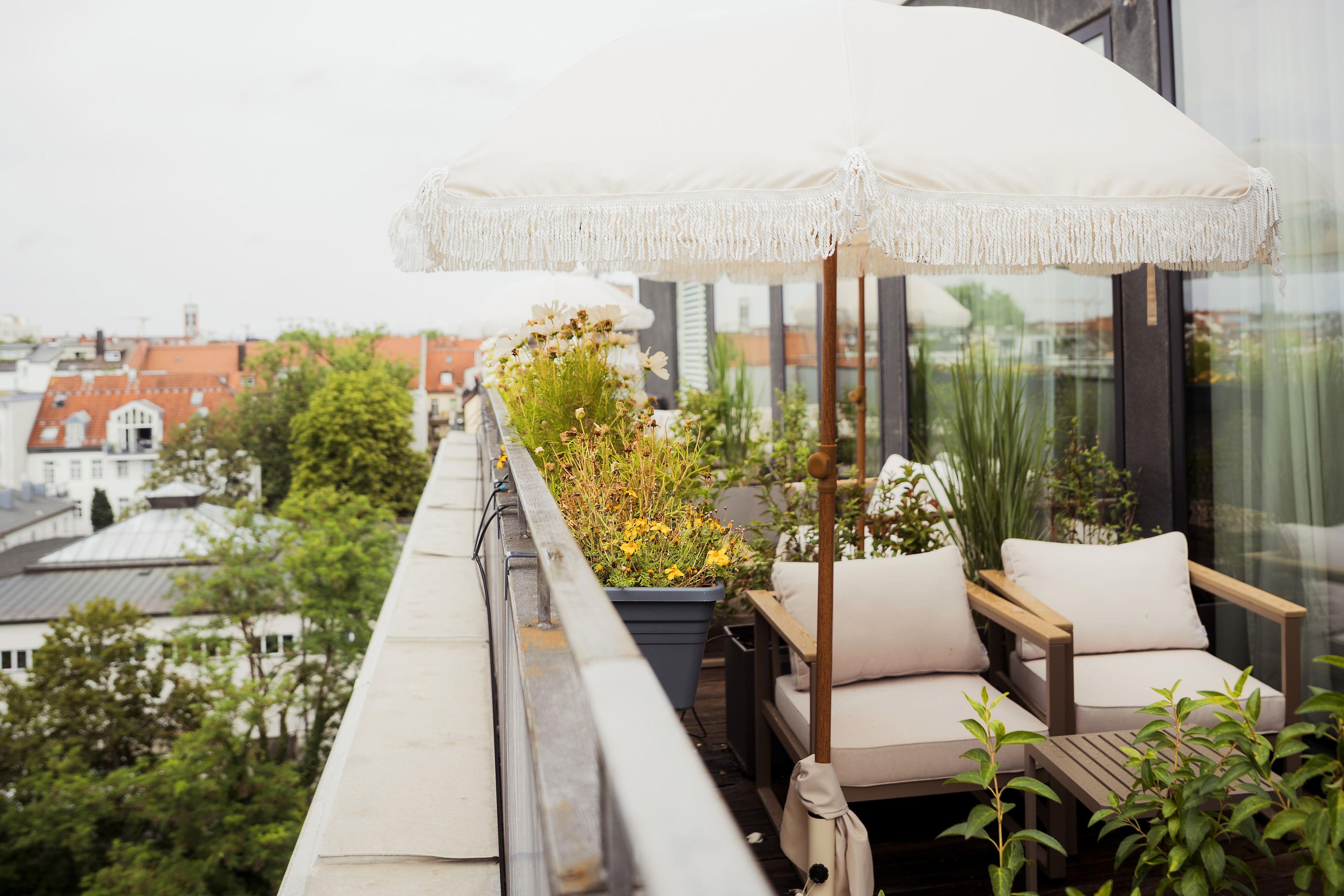 A balcony with a white umbrella, a potted plant, and a wooden chair.