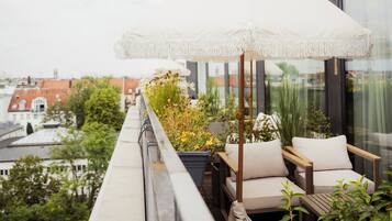 A balcony with a white umbrella, a potted plant, and a wooden chair.