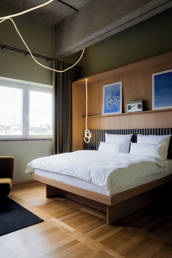 A modern hotel room with a large bed, wooden headboard, and a city view through the window. - ALPAMI Glockenbach  (Munich)