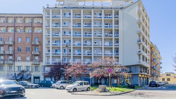 A multi-story residential building with balconies, a parking area, and a small garden with flowering trees. - This large studio apartment is ideally located for exploring Turin, with easy access to the subway, allowing you to reach the city center in just a few minutes and the lively San Salvario neighborhood in even less time. Just steps from Parco del Po, the  (Turin)