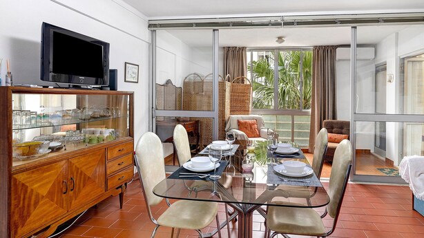 Un comedor con mesa de vidrio, sillas y un televisor sobre un mueble de madera.