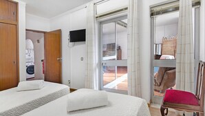 Habitación de hotel con dos camas, un televisor, una puerta corrediza al exterior y una silla de mimbre.
