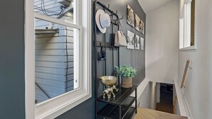 Corredor com um suporte de metal para chapéus e bolsas, uma tigela fixada na parede e quadros emoldurados.