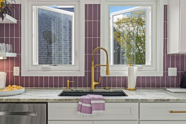 A kitchen with a marble countertop, gold faucets, and purple tiles.