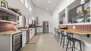 Uma cozinha moderna com armários brancos, uma geladeira de aço inoxidável e um espaço bar com banquetas.