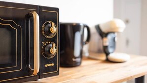 A microwave with two dials, a black mug, and a coffee maker on a wooden surface. - The Felix Piyat (Bourges)