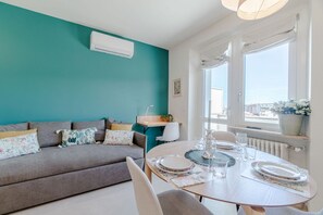 Ein modernes Wohnzimmer mit türkisfarbenen Wänden, einem grauen Sofa, einem Esstisch mit Tellern und Gläsern sowie einem Fenster mit Blick.