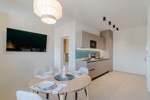 Ein zeitgemäßer Essbereich mit einem runden Tisch für vier Personen, eine Küche mit blauer Küchenrückwand und ein an der Wand befestigter Flachbildfernseher.