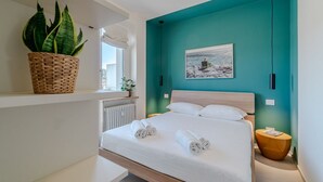 Ein modernes Schlafzimmer mit einer Türkis-farbenen Akzentwand, einem großen Bett mit weißen Leinen, einem gewebten Pflanzenkorb und einem gerahmten Bild.