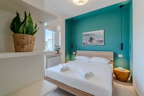 Ein modernes Schlafzimmer mit einer Türkis-farbenen Akzentwand, einem großen Bett mit weißen Leinen, einem gewebten Pflanzenkorb und einem gerahmten Bild.
