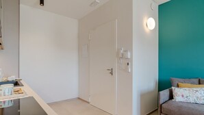 Ein modernes Zimmer mit Küchenzeile, einem Bett mit floralen Kissen, einer Türkis-farbenen Akzentwand und einer Tür mit Telefon und Lichtschalter.