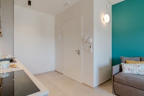 Ein modernes Zimmer mit Küchenzeile, einem Bett mit floralen Kissen, einer Türkis-farbenen Akzentwand und einer Tür mit Telefon und Lichtschalter.