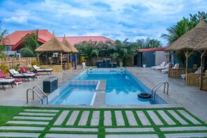 A swimming pool with lounge chairs, a thatched-roof structure, and a building with a red roof. - FFA Resort Center (Akure)