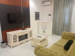 Ένα σαλόνι με τηλεόραση, μια λευκή βιβλιοθήκη, ένα τραπεζάκι σαλονιού και έναν καναπέ.