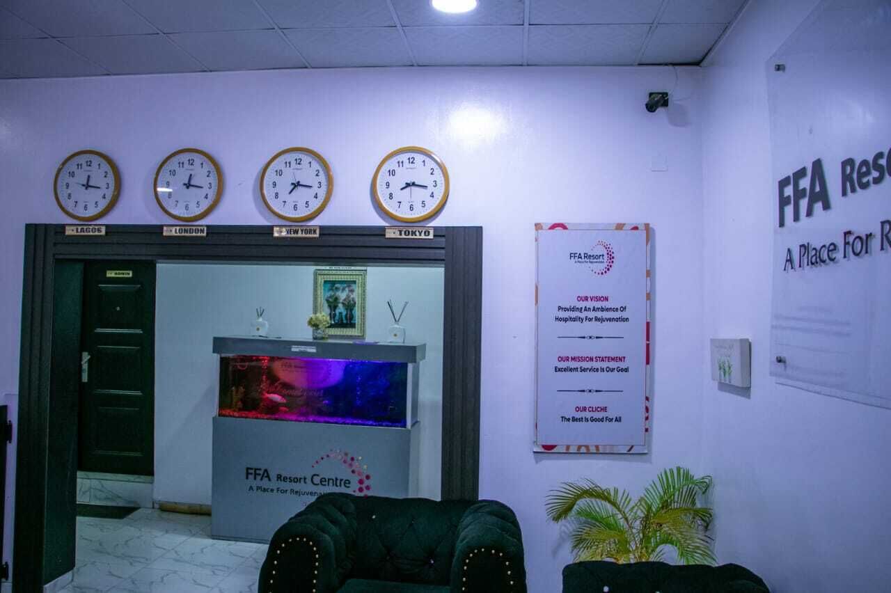 A reception area with clocks indicating different time zones, a reception desk, and a poster detailing the FFA Resort's mission and services.