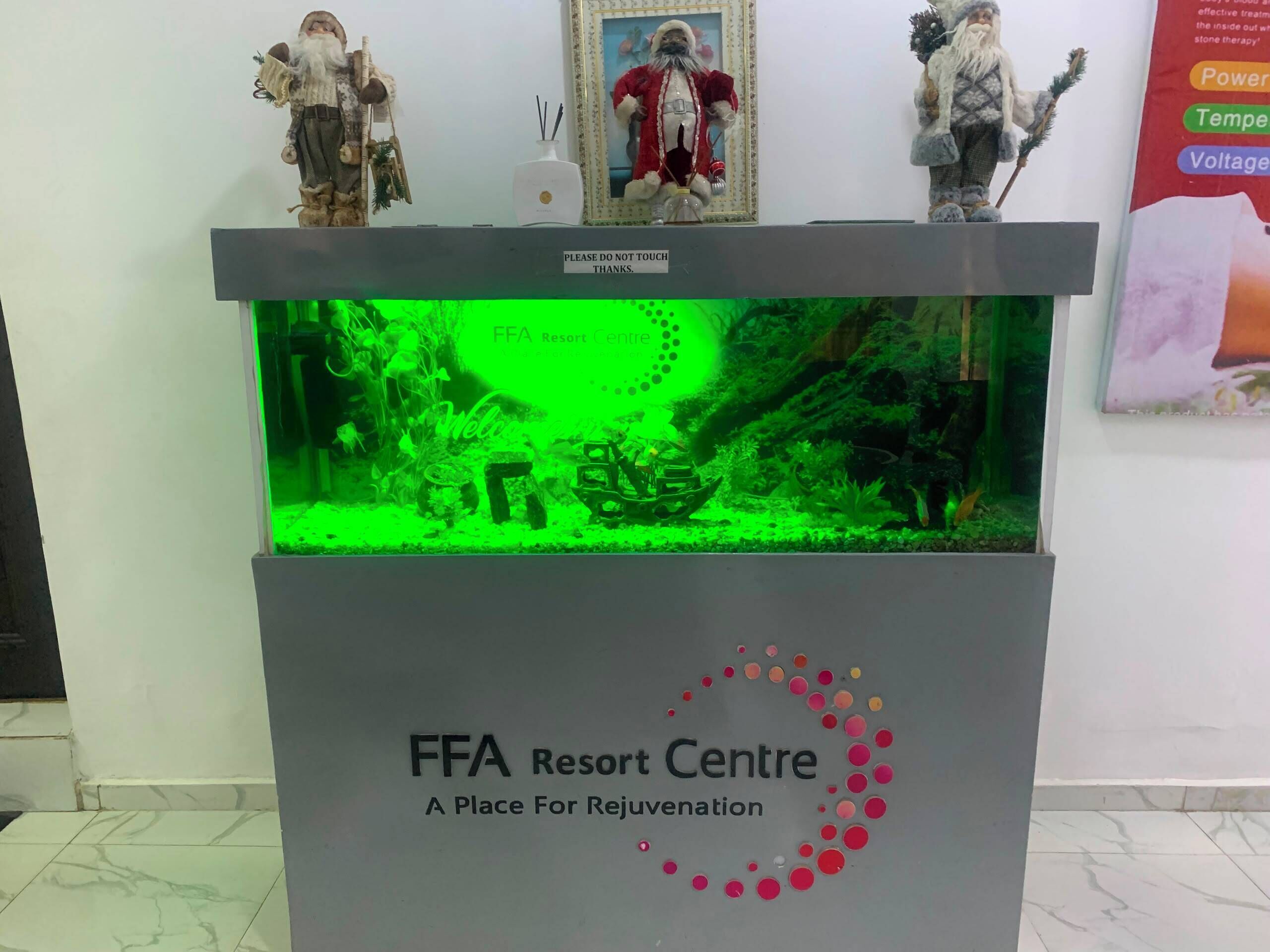 Un mostrador de recepción con un acuario iluminado en verde, un letrero que dice 'FFA Resort Centre' y figuras decorativas.