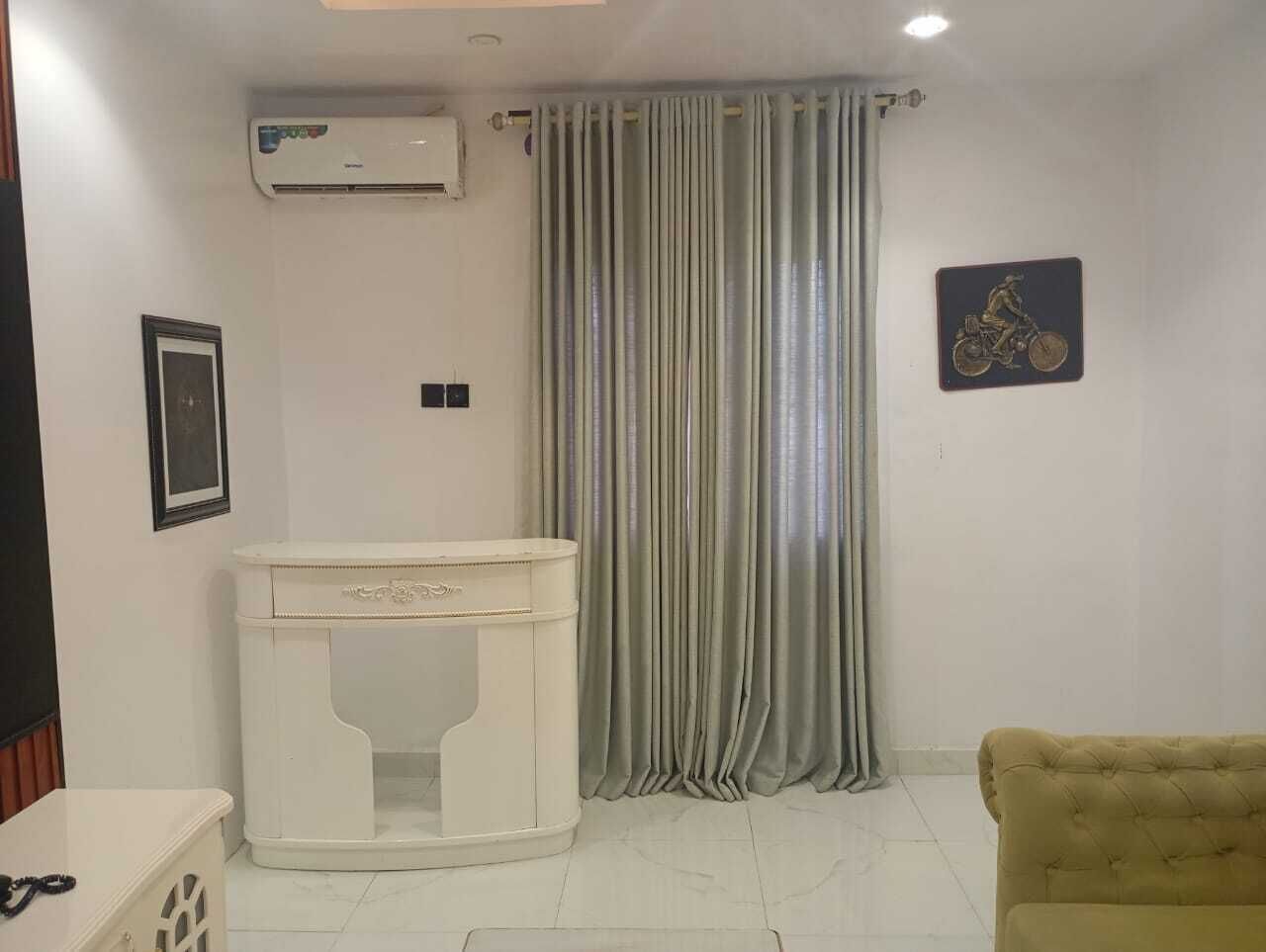 A room with a white air conditioning unit, a white pedestal, a grey curtain, a framed picture, and a tufted sofa.